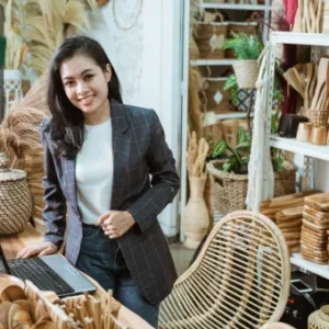 An entrepreneur in a craft workshop, standing confidently beside a laptop, surrounded by handmade wooden items.