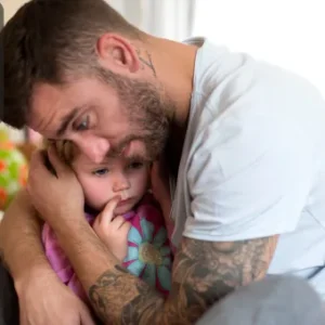 A concerned father holding and comforting his young child in a protective embrace, showing care and reassurance in a home environment.