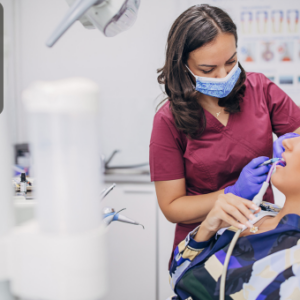 A dental hygienist wearing a mask and gloves performs a cleaning procedure on a female patient in a modern dental clinic.