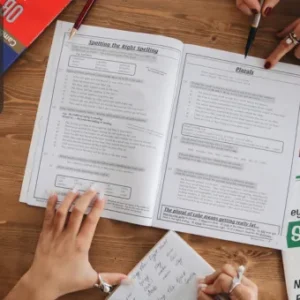 An open workbook on spelling and punctuation with hands taking notes and pointing at exercises, surrounded by educational books and study materials.