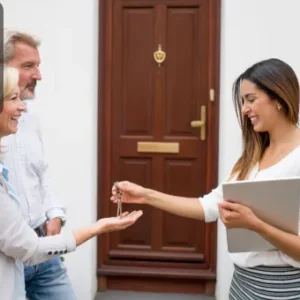 A smiling estate agent handing over house keys to a happy couple standing outside a front door.