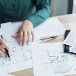 An architect working on building plans with design tools, sketches, and colour palettes on a desk.