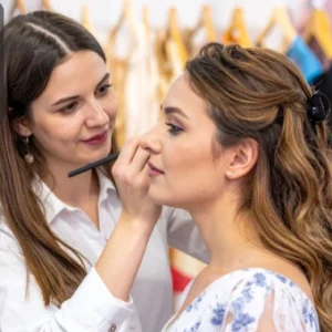 Makeup artist applying lipstick to a woman preparing for a bridal look.