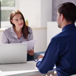 A professional woman reviewing tax documents with a client across the desk in a bright office, featuring the Thames College logo in the top-left corner.