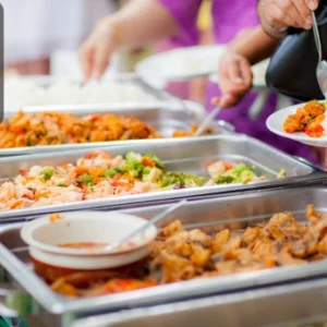 Guests serving themselves from buffet trays filled with a variety of colourful dishes at a catering event. The Thames College logo appears in the corner.