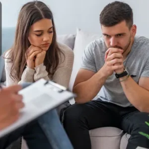 A couple sitting together in a therapy session with a counsellor, showing concern and reflection.