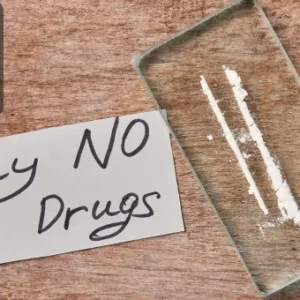 A handwritten note reading “Say NO to Drugs” placed next to a tray containing white powder resembling drug lines, on a wooden surface.