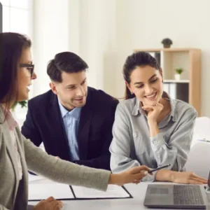 Three professionals in an office environment discussing estate management, looking at a laptop screen with interest.