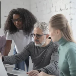 A diverse group of professionals collaborating around a laptop, discussing data and information management in a modern office setting.