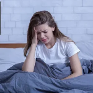 Distressed young woman sitting up in bed with her head in her hand, displaying signs of emotional strain, stress, or anxiety.