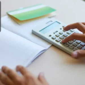 A close-up of a person using a calculator and referencing a ledger book, symbolising financial record-keeping and purchase ledger management.