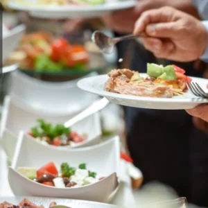 Guests serving themselves from a buffet table filled with various salads and main dishes at a catering event. The Thames College logo appears in the corner.