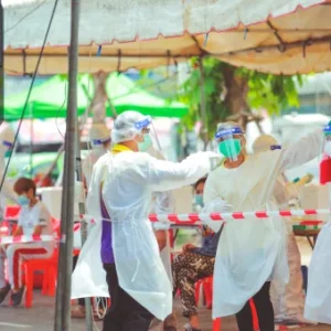 Public health workers in full PPE conducting health screenings at an outdoor medical tent.