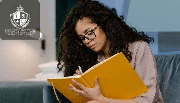 A woman with curly hair and glasses sits on a sofa, attentively writing in a large yellow notebook; Thames College logo appears in the top-left corner.