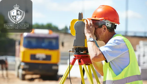 A construction surveyor wearing a high-visibility vest and hard hat uses a theodolite on a tripod to measure distances at a building site, with a truck in the blurred background.