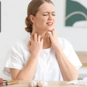 A woman experiencing an allergic reaction, holding her throat in discomfort, seated at a kitchen table with food ingredients around her.