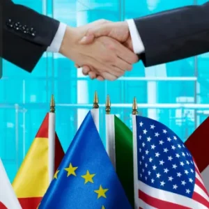 Two individuals shaking hands above a row of international flags, with the Thames College logo in the top left corner.