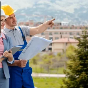 Two construction professionals wearing safety helmets, one holding blueprints and the other holding a tablet, standing outdoors and discussing a property site, with the Thames College logo in the top left corner.