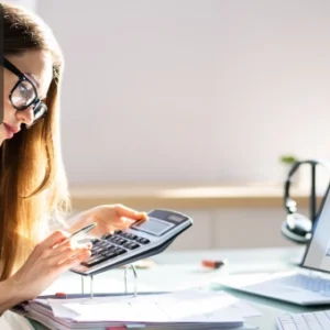 Woman working on a calculator and reviewing invoices on a laptop, symbolising attention to detail in accounts payable.